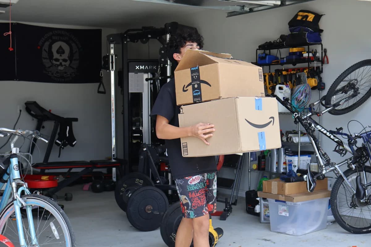 A crew member carrying two stacked cardboard boxes out of a garage