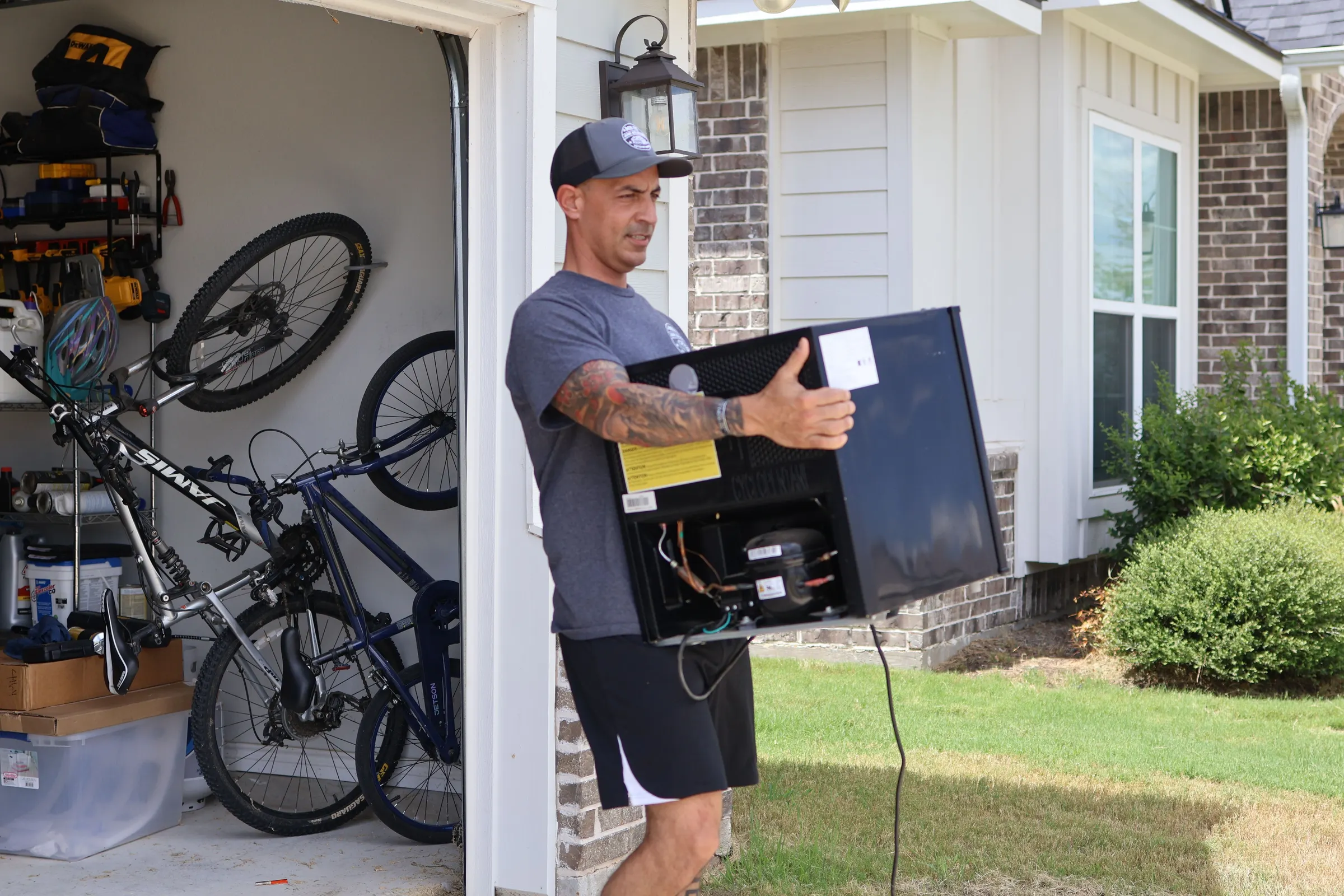 Eddie carrying a small black refrigerator out of a garage, the kind of job we do in Iola, TX