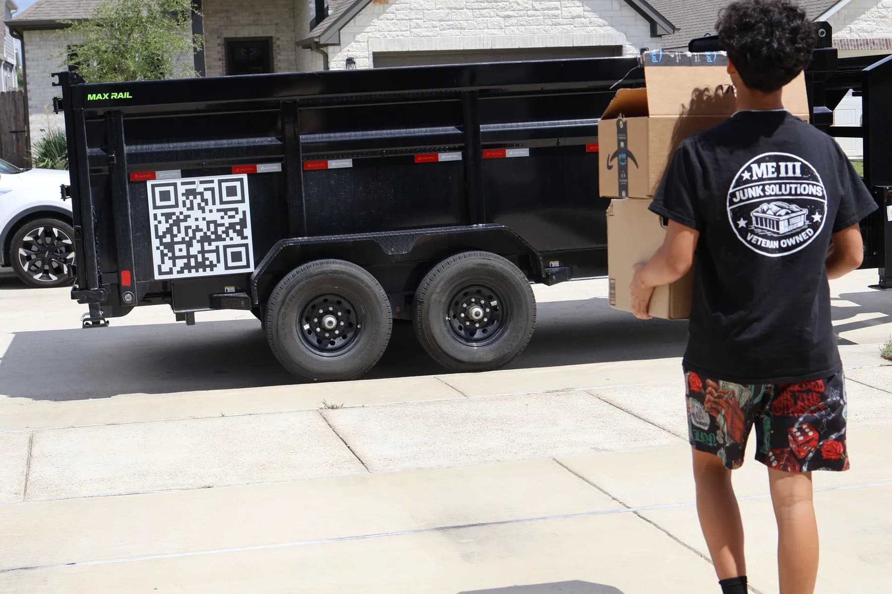 An ME3 Junk Solutions crew member carrying a box to the black dump trailer in a driveway