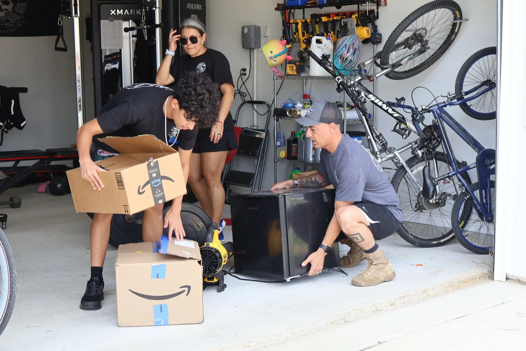 Three people in ME3 Junk Solutions shirts moving a mini fridge and boxes out of a garage